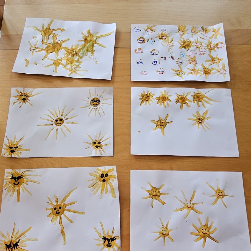 A collection of six white papers with yellow sun designs on a wooden table. Each sun has a face with different expressions.