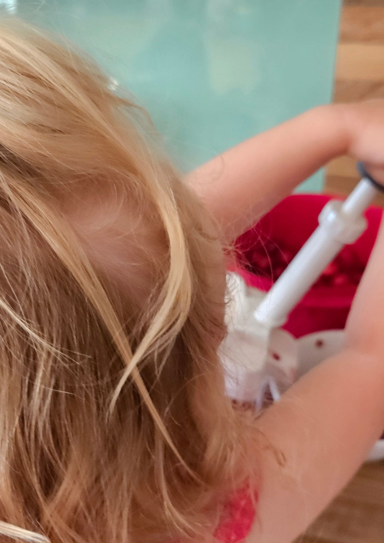 Ein Kind mit blonden Haaren hält einen roten Korb, wahrscheinlich in einem Badezimmer. Der Korb ist mit Gegenständen gefüllt.