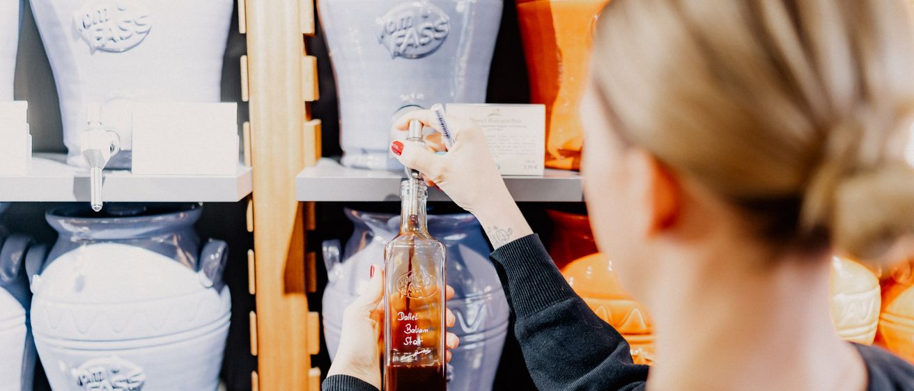 Eine Frau hält eine Flasche Dalzell Balsamico-Essig in einem Geschäft, umgeben von verschiedenen Gläsern.