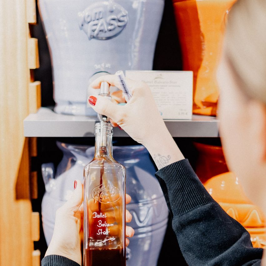 Eine Frau hält eine Flasche Dalzell Balsamico-Essig in einem Geschäft, umgeben von verschiedenen Gläsern.