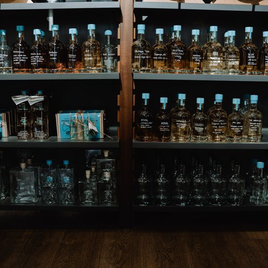 Ein hölzerne Regalreihe zeigt verschiedene Spirituosenflaschen, wobei sich unten klare Glasflaschen und oben bernsteinfarbene Flaschen befinden.