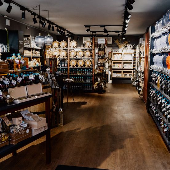 Ein Ladeninnenraum mit Holzböden, Regalen voller Produkte, Fässern und Dekorationsartikeln. Scheinwerfer hängen von der Decke.