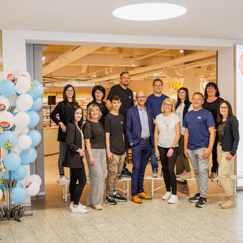 Eine Gruppe von Menschen, die für ein Foto in einem Geschäft mit Luftballons, einer Decke und Regalen im Hintergrund posiert.