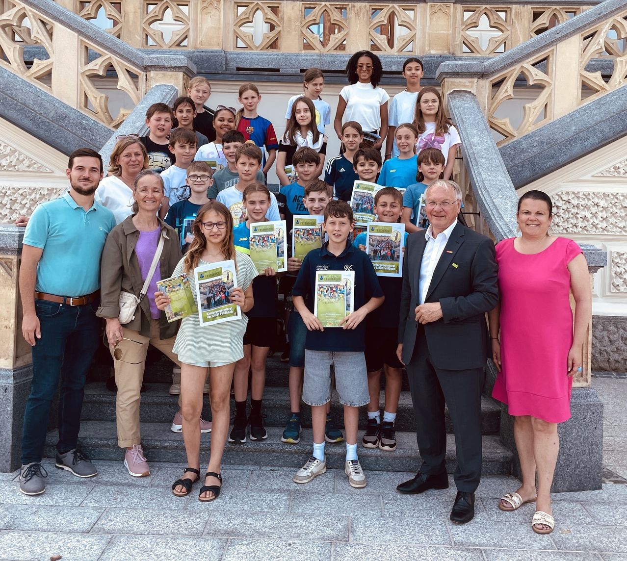 Eine Gruppe von Kindern und Erwachsenen posiert für ein Foto auf einer Treppe und hält Bücher in den Händen. Sie alle lächeln für die Kamera.
