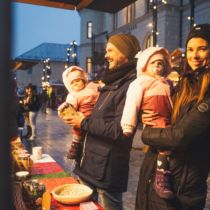 Ein Mann und eine Frau halten zwei Babys in der Nacht auf einem festlichen Markt. Sie lächeln und halten die Kinder eng umschlungen.