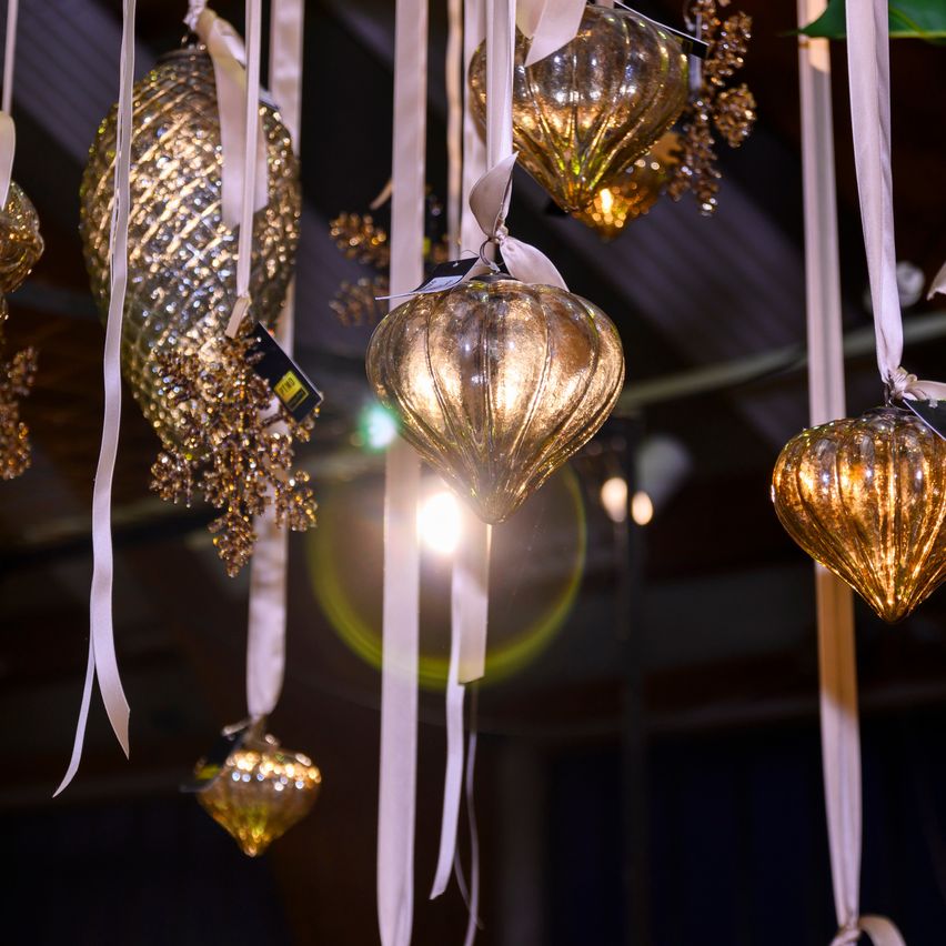 A close-up view of several golden glass ornaments hanging from white ribbons in a dark room. The ornaments are shiny and have a shiny effect. A bright light is illuminating the ornaments.