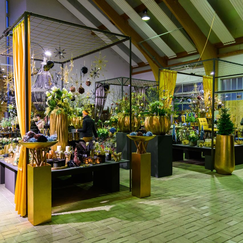 A garden display with golden pots, decorative plants, and ornaments. People explore the area, which is enclosed by yellow curtains.
