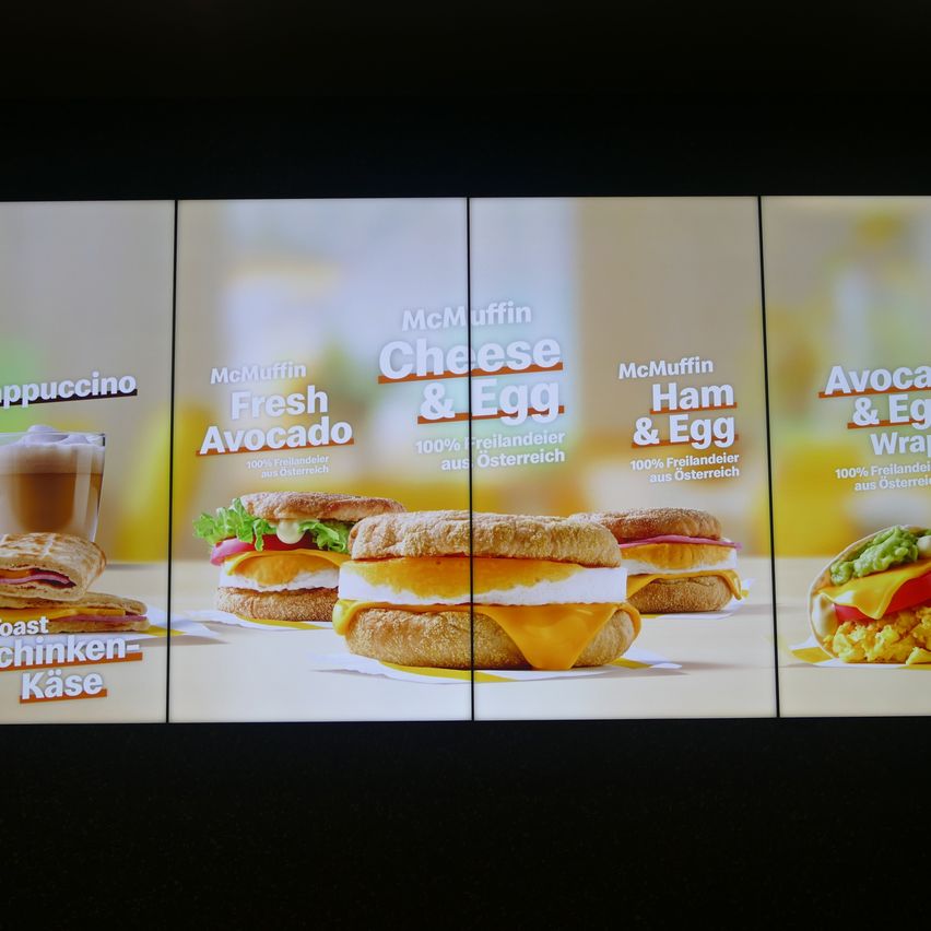 Menu board displaying breakfast options: McMuffin Cappuccino, Fresh Avocado McMuffin, Cheese & Egg McMuffin, Ham & Egg McMuffin, and Avocado & Egg Wrap.