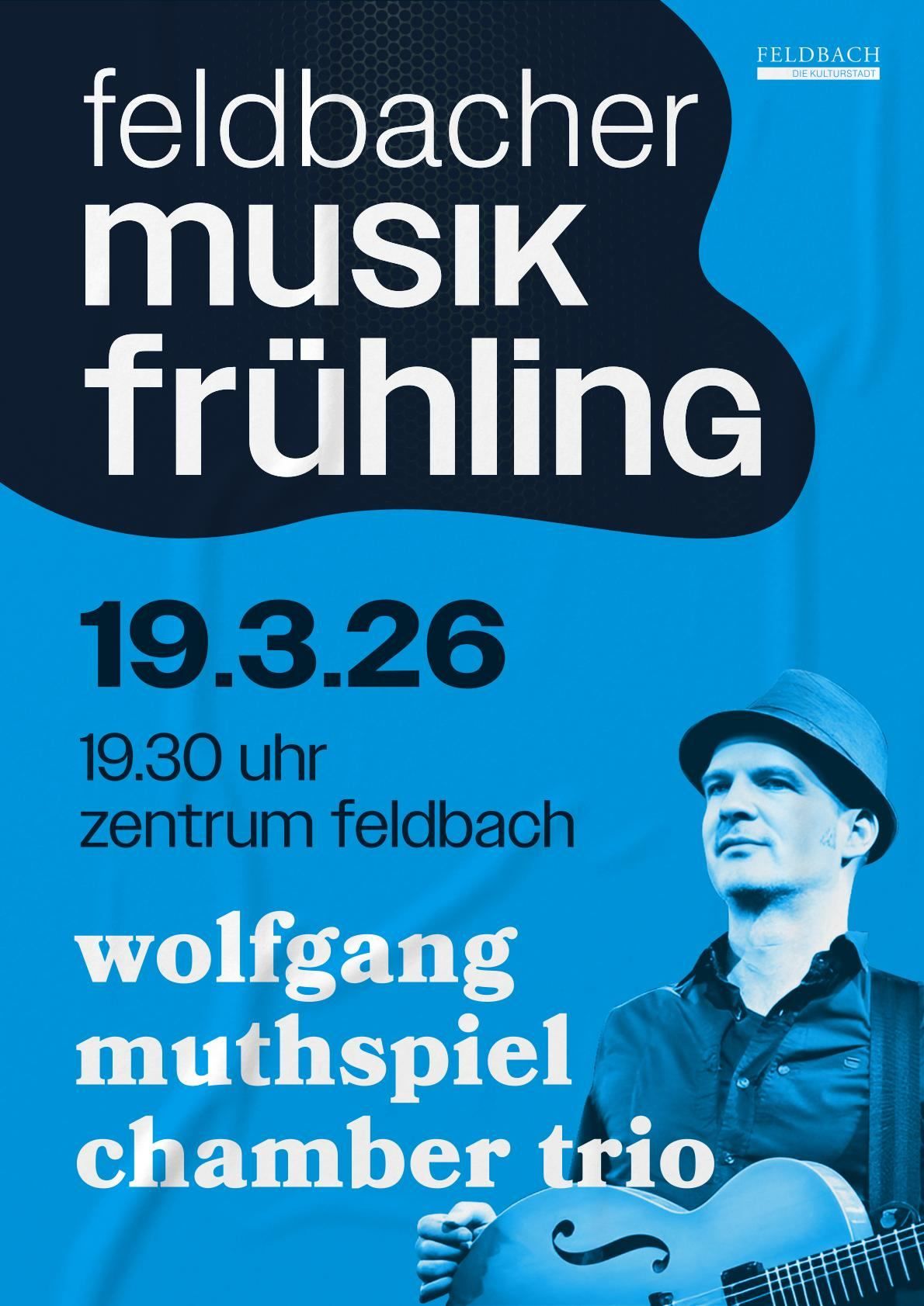 Blaues Plakat für Wolfgang Muthspiels Musik Frühling Veranstaltung. Datum: 19. März 2026, Zeit: 19:30. Ort: Zentrum Feldbach. Ein Mann in einem Hut ist auf der rechten Seite abgebildet.