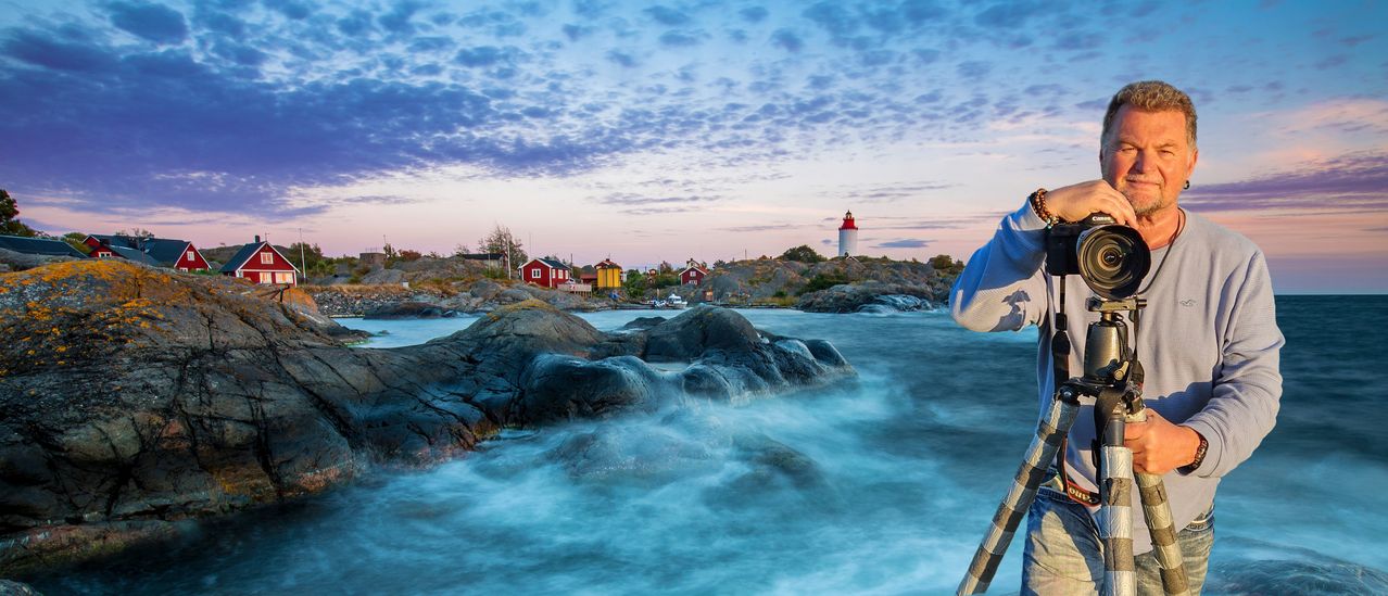 Malerische Aussicht auf eine felsige Küstenlinie mit bunten Häusern, einem Leuchtturm und einem blauen Himmel mit Wolken.