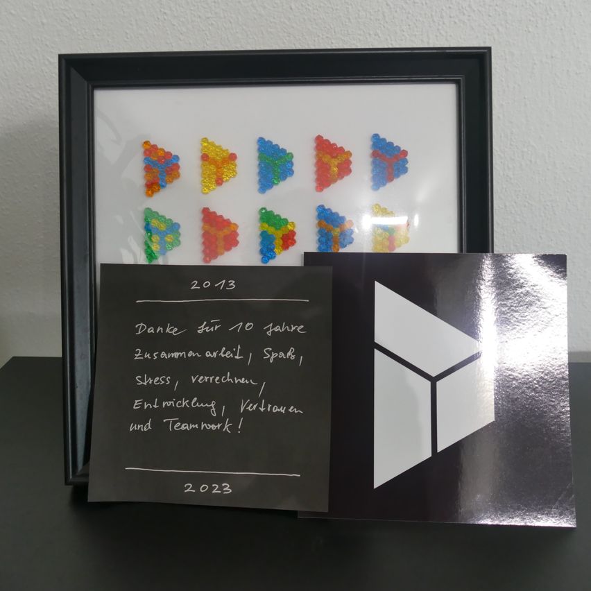 Ein gerahmtes Kunstwerk mit farbenfrohen Perlenmosaiken an einer Wand, begleitet von einem Dankesschreiben für 10 Jahre Zusammenarbeit.