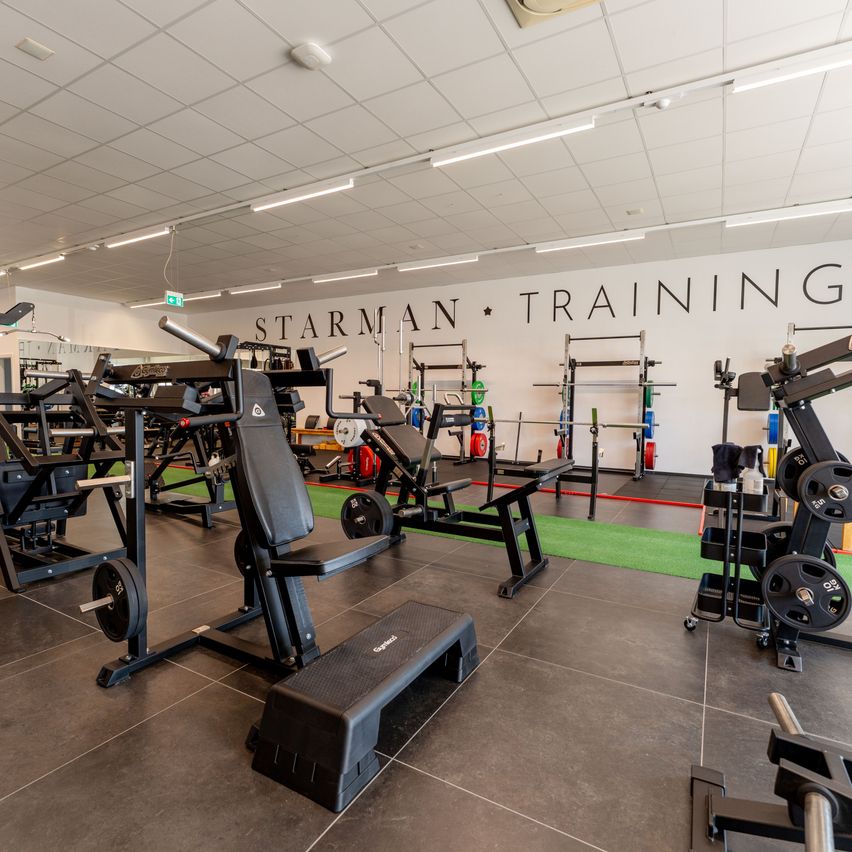A well-lit gym with various exercise equipment and a large white wall with the words 'Starman Training' written on it.