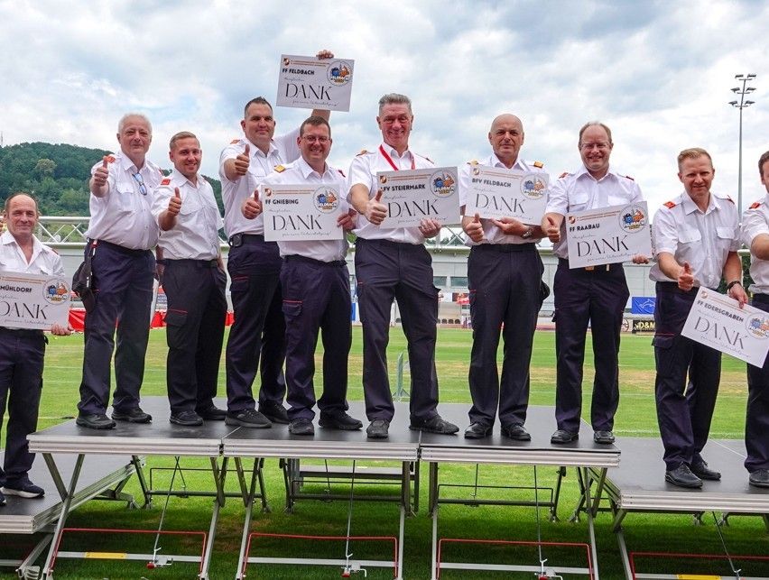 A group of uniformed individuals stand on a stage, holding signs that read 'Dank'. They appear to be celebrating an achievement.