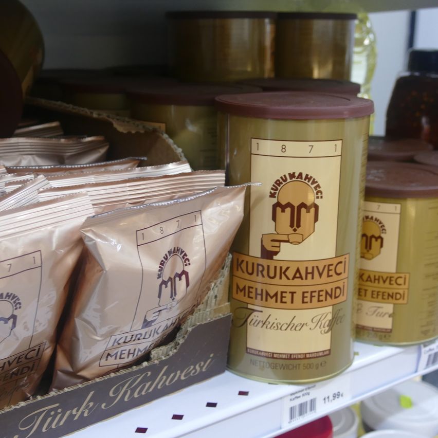 Ein Regal zeigt mehrere Dosen und Tüten Kaffee. Eine prominente Dose ist mit 'Kurukahvecil Mehmet Efendi Türkischer Kaffee' beschriftet. Andere Artikel sind ebenfalls sichtbar.