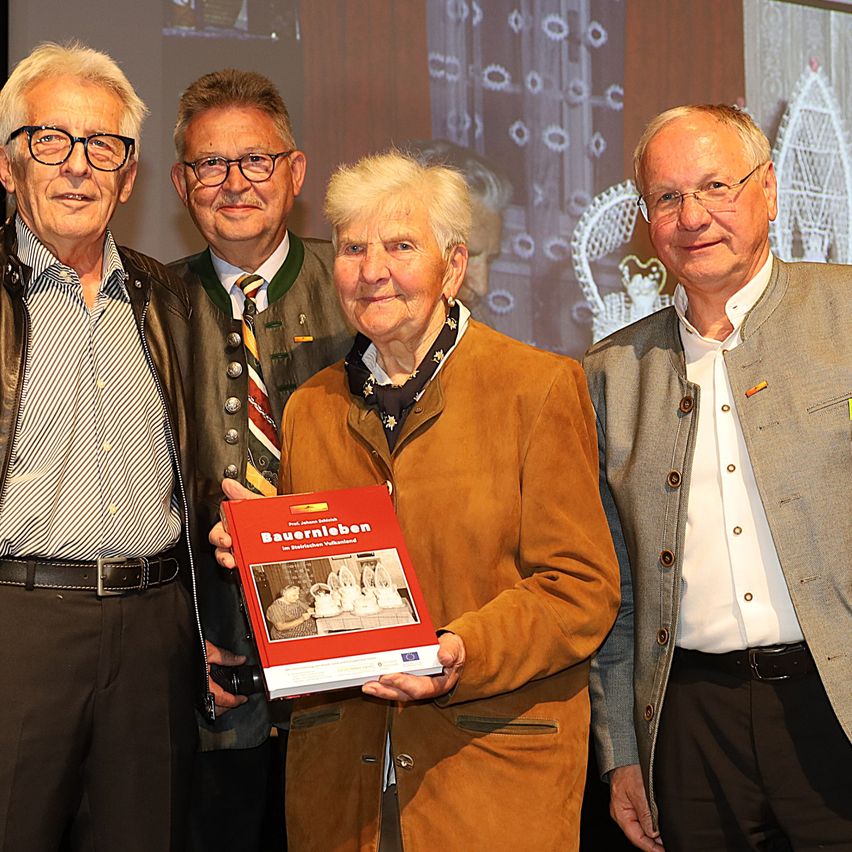 Vier Männer stehen zusammen, einer hält ein Buch. Sie scheinen bei einer Preisverleihung zu sein. Das Buch ist rot mit dem Titel 'Bauernleben'.