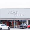 Die Vorderseite des Auto Pieber-Händlers zeigt mehrere Autos, die vor dem Gebäude geparkt sind, darunter ein Hyundai und ein roter Kia. Das Gebäude hat eine graue Außenfassade mit weißen Texten und Logos.