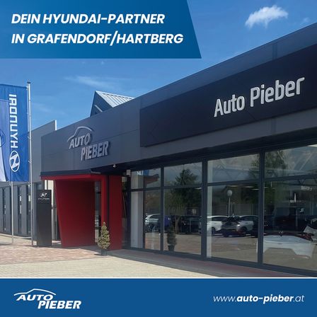 Die Fassade eines Auto Pieber-Händlers, ein Hyundai-Partner in Grafendorf/Hartberg, zeigt eine moderne Glasfassade und eine blaue Fahne.