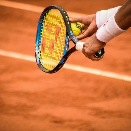 Ein Tennisspieler hält einen Tennisschläger mit einem Tennisball, bereit zum Schlagen auf einem Sandplatz.