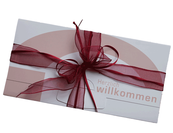 Eine weiße Karte mit einem roten Band und einer Botschaft, die 'Herzlich willkommen' in einer stilisierten Schrift sagt, wahrscheinlich zur Begrüßung von jemandem gedacht.