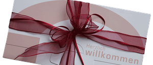 Eine weiße Karte mit einem roten Band und einer Botschaft, die 'Herzlich willkommen' in einer stilisierten Schrift sagt, wahrscheinlich zur Begrüßung von jemandem gedacht.