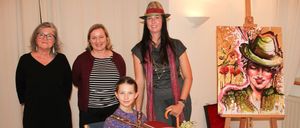 Vier Frauen und ein junges Mädchen posieren für ein Foto in einem Raum. Das Mädchen hält ein Akkordeon. Hinter ihnen steht ein Staffelei mit einem Gemälde einer Frau in einem Hut.