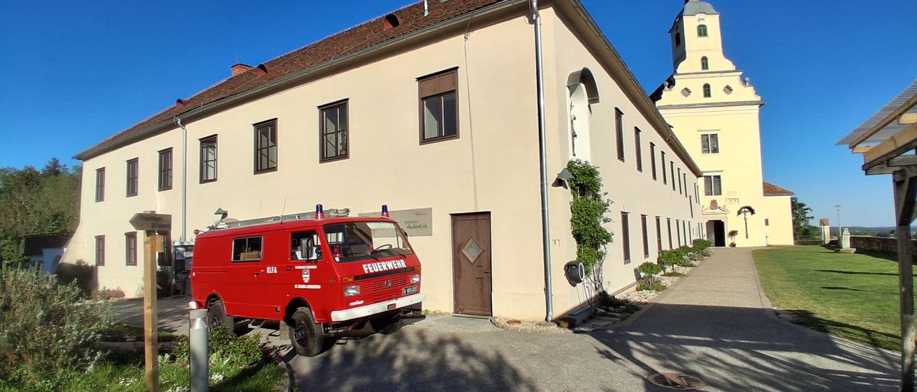 Ein roter Feuerwehrwagen steht vor einem großen Gebäude mit vielen Fenstern und einer braunen Tür.