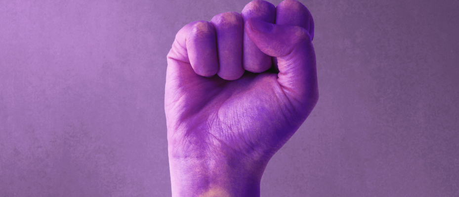 Eine in Lila gemalte Hand mit einem weiblichen Symbol auf dem Handgelenk, erhoben in einer Faust vor einem lila Hintergrund.