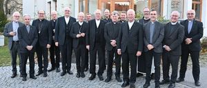 Eine Gruppe von Priestern und Bischöfen in formellen schwarzen Anzügen und einigen mit Kreuzen posiert für ein Foto vor einem Gebäude.