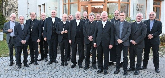 Eine Gruppe von Priestern und Bischöfen in formellen schwarzen Anzügen und einigen mit Kreuzen posiert für ein Foto vor einem Gebäude.
