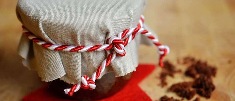 Ein mit Stoff umwickelter und mit rot-weißer Schnur gebundener Glaskrug liegt auf einem roten Stern. Es steht auf einer hölzernen Oberfläche mit einigen Krümeln herum.