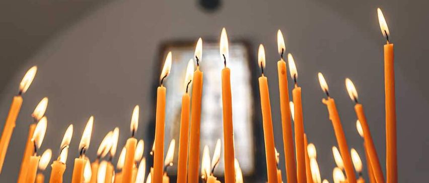 Viele gelbe Kerzen sind in einer Kirche angezündet, mit einem Bilderrahmen im Hintergrund.