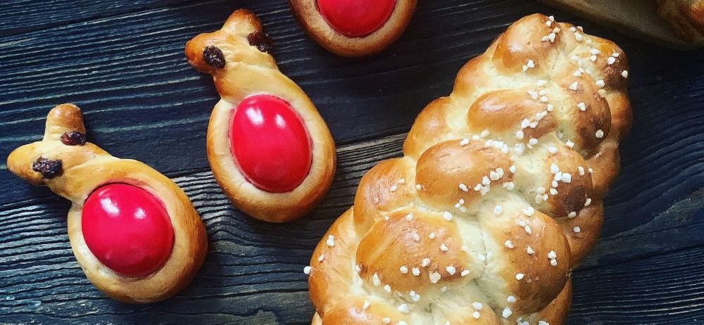 Ein Nahaufnahme einer Holztisch mit vier dekorierten Gebäckstücken darauf. Jedes Gebäck hat eine rote Füllung. Es gibt ein größeres Brot mit geflochtener Textur.