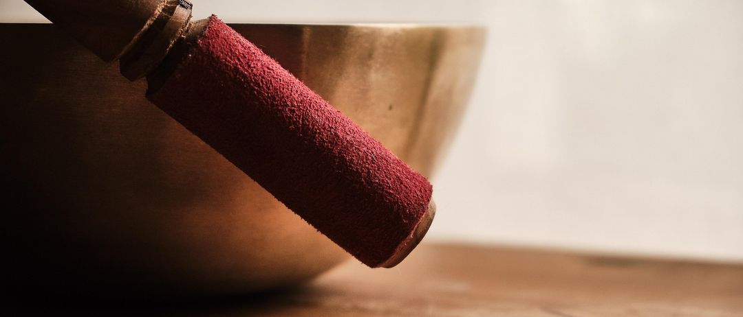 Ein roter Stab mit Samtbezug liegt auf einer goldfarbenen Schüssel, die auf einem hölzernen Tisch vor einem weißen Hintergrund platziert ist.
