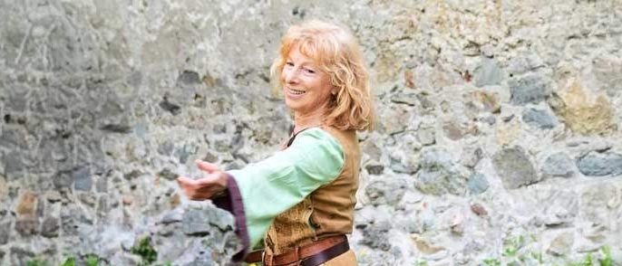Eine Frau in einem grünen und braunen Kostüm mit einem Schwert und einem Ledergürtel tanzt auf einem Rasen.