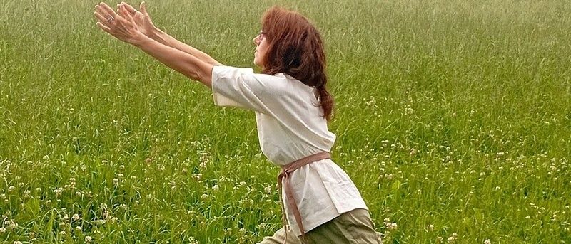 Eine Frau mit einem Ring am Finger steht in einem grasigen Feld und streckt ihre Arme nach oben.