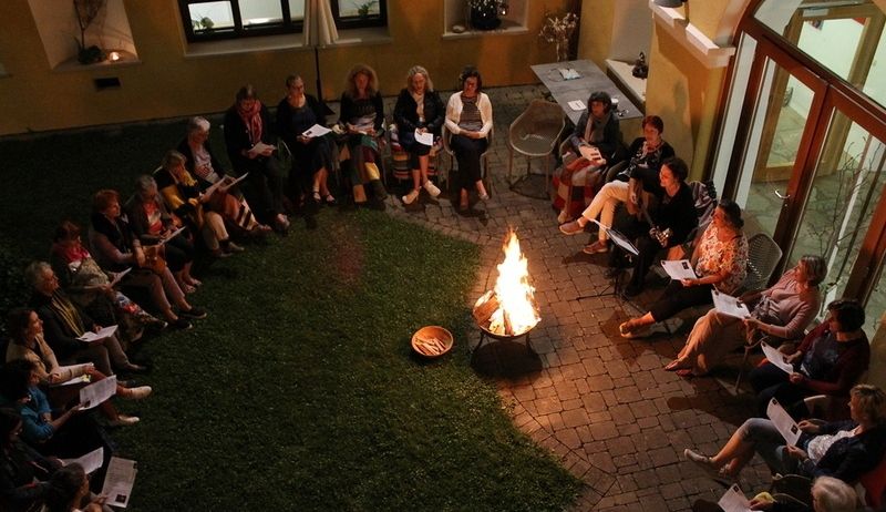 Eine Gruppe von Menschen sitzt im Kreis um ein Feuer herum und liest Bücher.