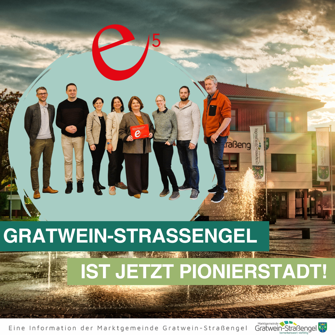 Eine Gruppe von Menschen steht vor einem Gebäude mit einem Springbrunnen und lächelt. Der Text lautet 'Gratwein-Straßengel ist jetzt eine Pionierstadt'.
