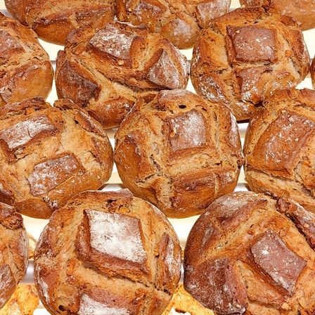 Eine Nahaufnahme mehrerer ganzer Laibe von braunem Brot mit einer knusprigen Kruste und einigen Scheiben darauf.