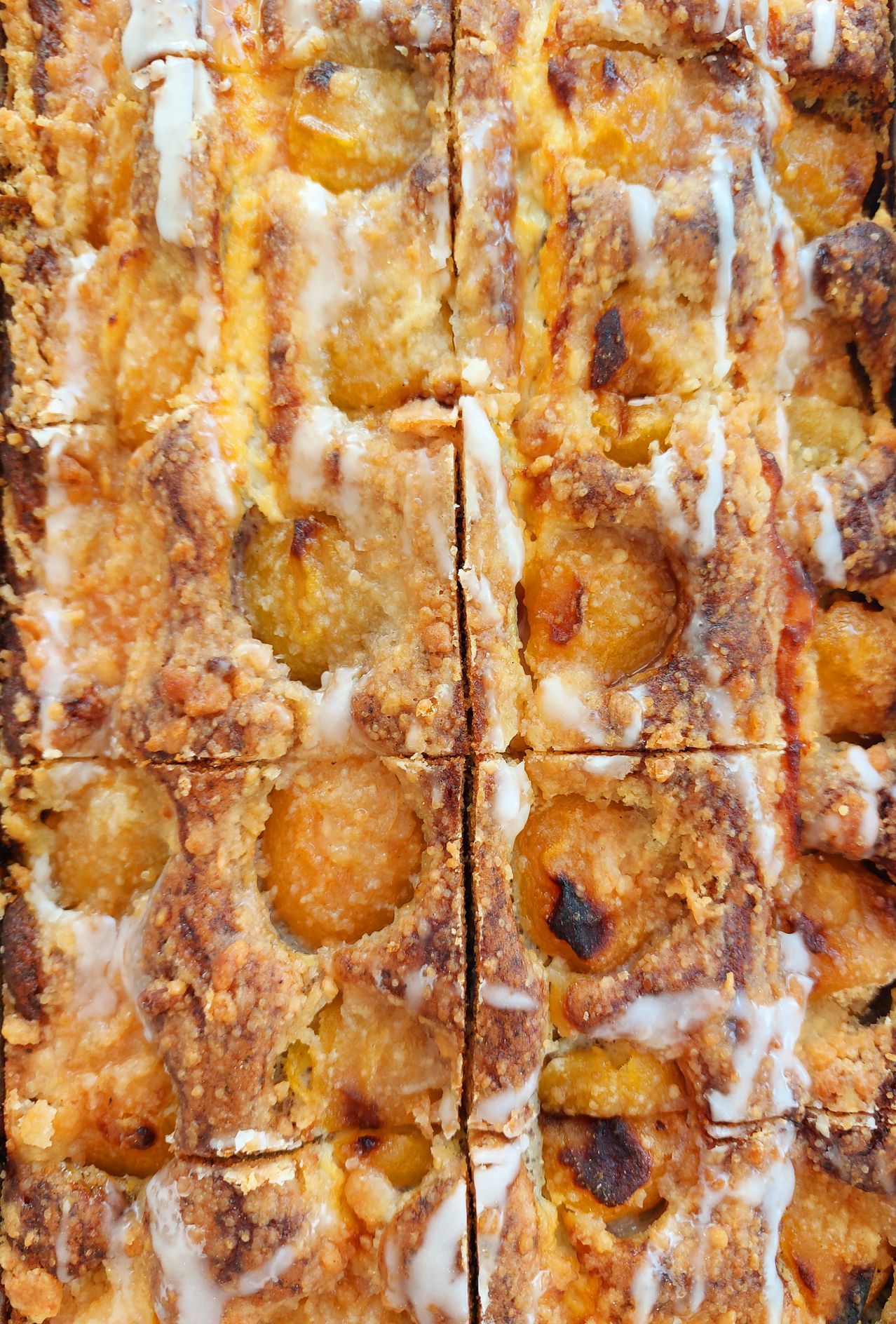 A close-up view of a square-shaped dessert with a golden-brown crust, filled with peach slices and topped with white icing.