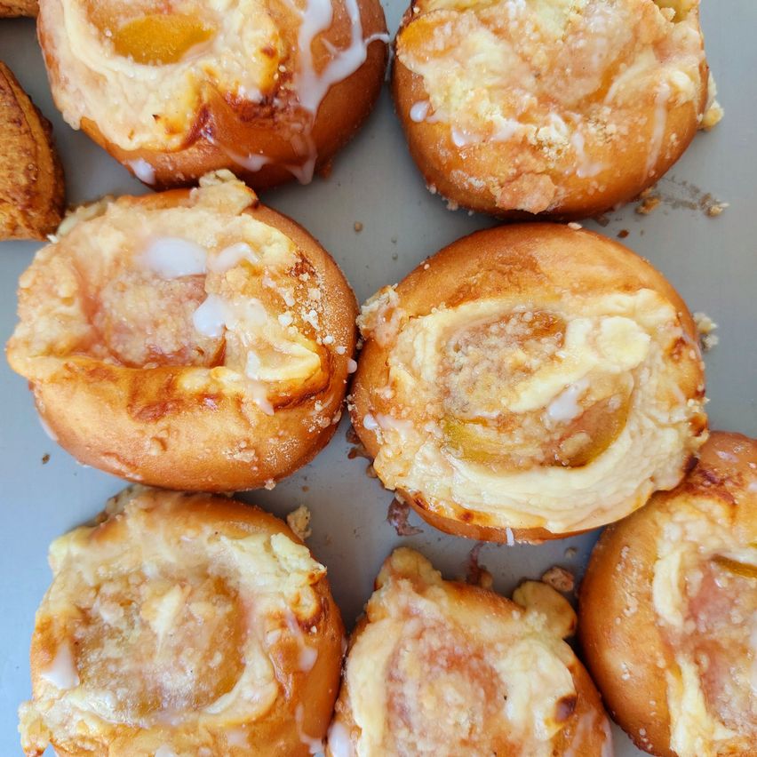 Close-up of several peach-filled pastries with a golden brown crust and a white icing swirl on top.