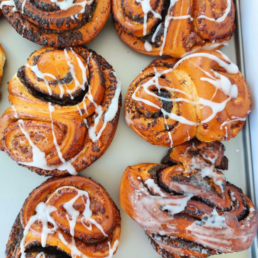 A tray of freshly baked cinnamon rolls with white icing, some with a swirl pattern on top.