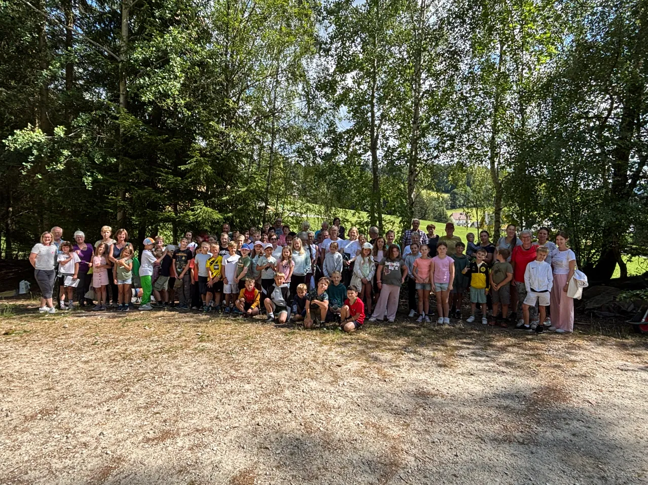 Eine Gruppe von Menschen in verschiedenen Outfits steht in einem Grasfeld mit Bäumen im Hintergrund.
