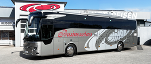 Ein silberner Bus mit der Aufschrift 'Businessclass by KOMET' vor einem Gebäude mit rotem Logo geparkt.