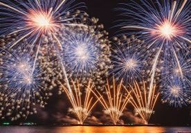 Mehrere Feuerwerke explodieren in der Nacht über einer Wasserfläche und reflektieren auf der Wasseroberfläche.