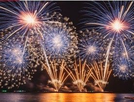 Mehrere Feuerwerke explodieren in der Nacht über einer Wasserfläche und reflektieren auf der Wasseroberfläche.