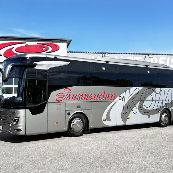 Ein großer grauer und roter Businessclass von KOMET Bus ist vor einem Gebäude mit einem roten Logo geparkt. Der Bus ist an einem klaren Tag.