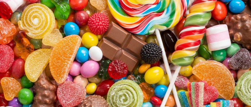 Eine bunte Auswahl an Süßigkeiten, einschließlich Lollipops, Schokoladen und Gummibärchen, in einem dekorativen Muster auf einem weißen Hintergrund angeordnet.