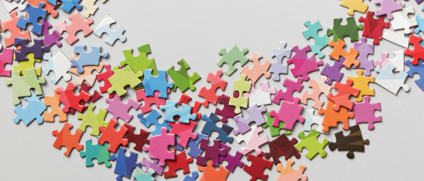 Eine bunte Auswahl an Puzzleteilen, die auf einer weißen Oberfläche verstreut sind und ein wellenförmiges Muster bilden.