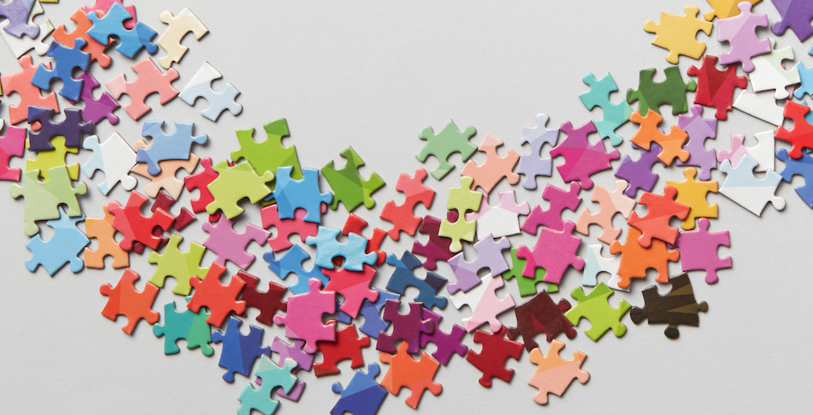 Eine bunte Auswahl an Puzzleteilen, die auf einer weißen Oberfläche verstreut sind und ein wellenförmiges Muster bilden.