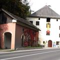 Zwei Gebäude mit unterschiedlichen Architekturstilen, eines mit einer roten Rebe und das andere mit einer Fahne, an einer Straße gelegen.